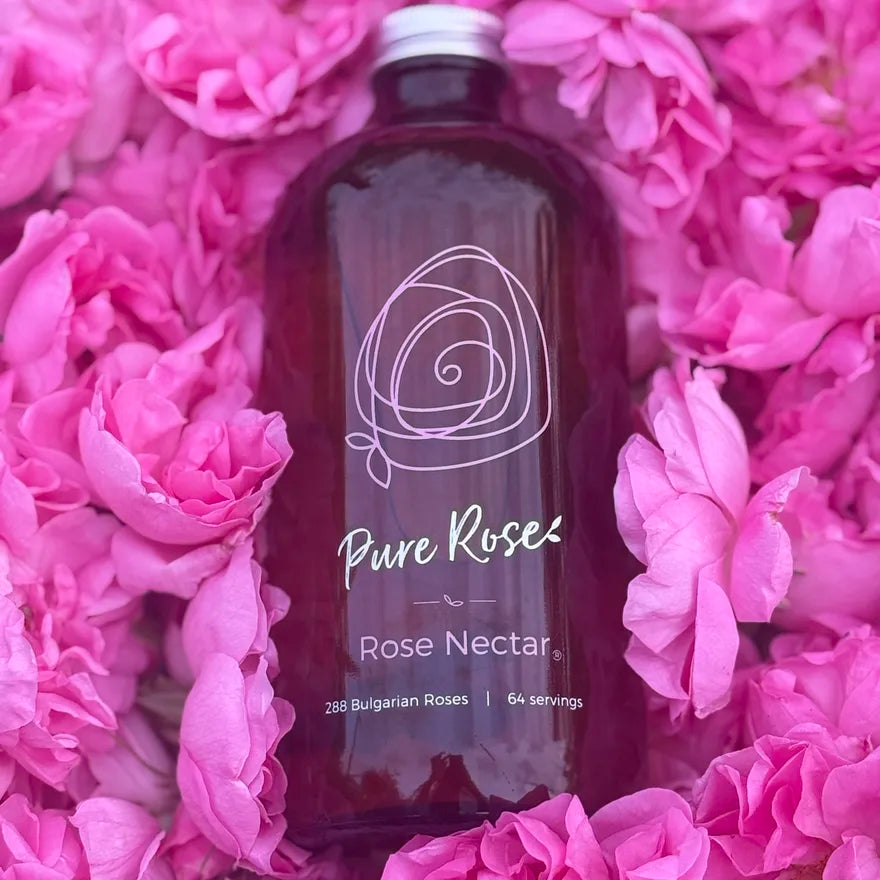 A 16oz amber bottle of Rose Nectar resting among freshly picked pink Bulgarian rose blooms