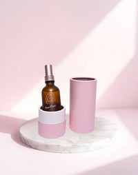 Rose Mist bottle in its open pink tube on a marble stand